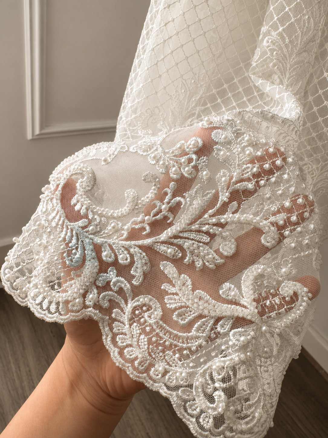 An elegant heirloom gown designed with timeless tradition in mind. Crafted from intricate lace, this gown features pearl and sequence embellishments throughout. It features delicate short sleeves, a softly structured bodice. The back is finished with delicate pearl buttons and a long mikado side belt that can be tied into a bow. The intricate lacework flows throughout the gown, creating beautiful texture and detail from every angle. 
