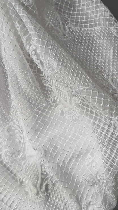An elegant heirloom gown designed with timeless tradition in mind. Crafted from intricate lace, this gown features pearl and sequence embellishments throughout. It features delicate short sleeves, a softly structured bodice. The back is finished with delicate pearl buttons and a long mikado side belt that can be tied into a bow. The intricate lacework flows throughout the gown, creating beautiful texture and detail from every angle. 