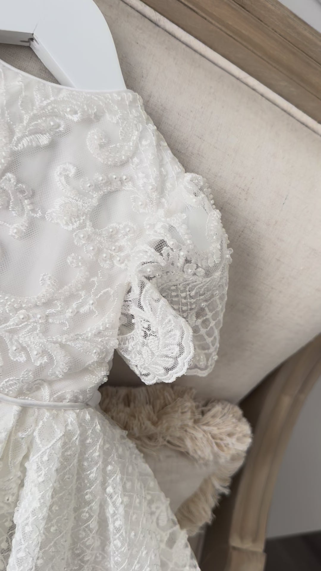 An elegant heirloom gown designed with timeless tradition in mind. Crafted from intricate lace, this gown features pearl and sequence embellishments throughout. It features delicate short sleeves, a softly structured bodice. The back is finished with delicate pearl buttons and a long mikado side belt that can be tied into a bow. The intricate lacework flows throughout the gown, creating beautiful texture and detail from every angle. 