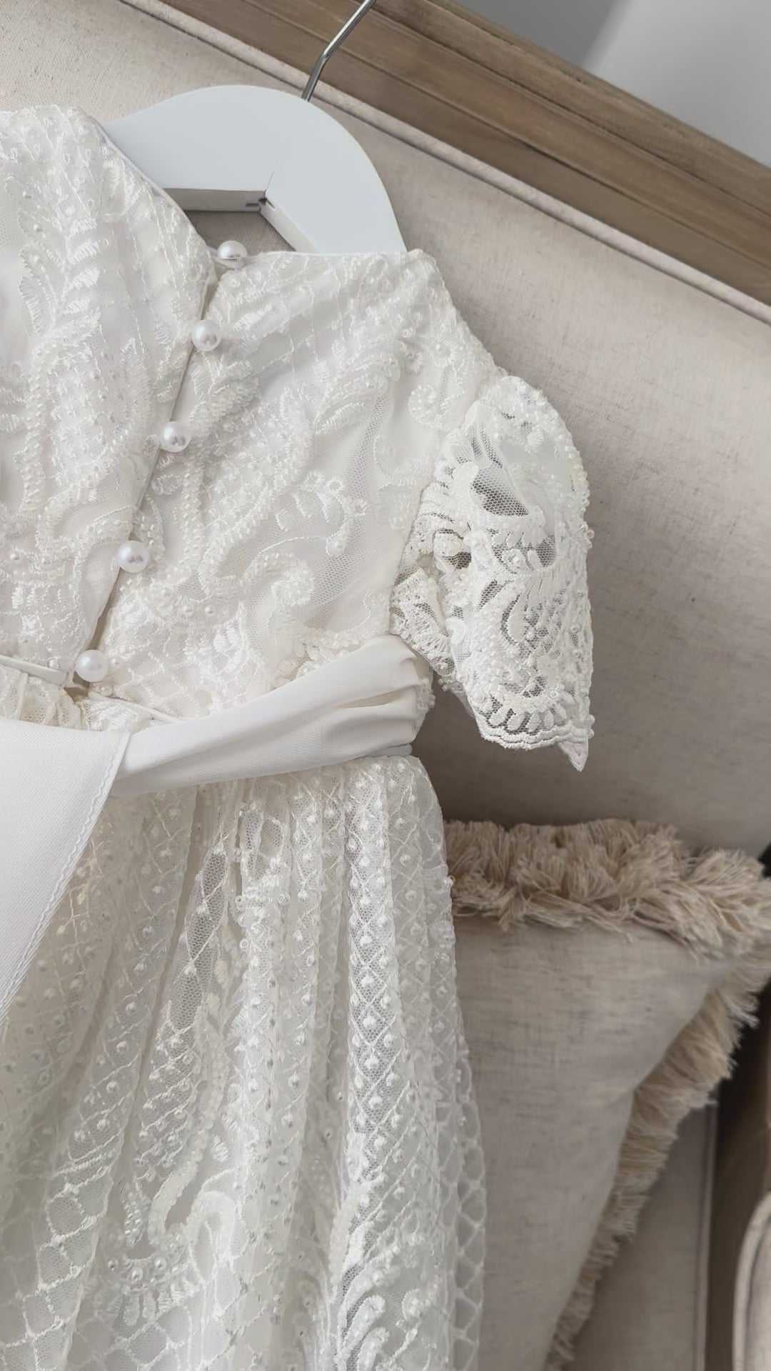 An elegant heirloom gown designed with timeless tradition in mind. Crafted from intricate lace, this gown features pearl and sequence embellishments throughout. It features delicate short sleeves, a softly structured bodice. The back is finished with delicate pearl buttons and a long mikado side belt that can be tied into a bow. The intricate lacework flows throughout the gown, creating beautiful texture and detail from every angle. 
