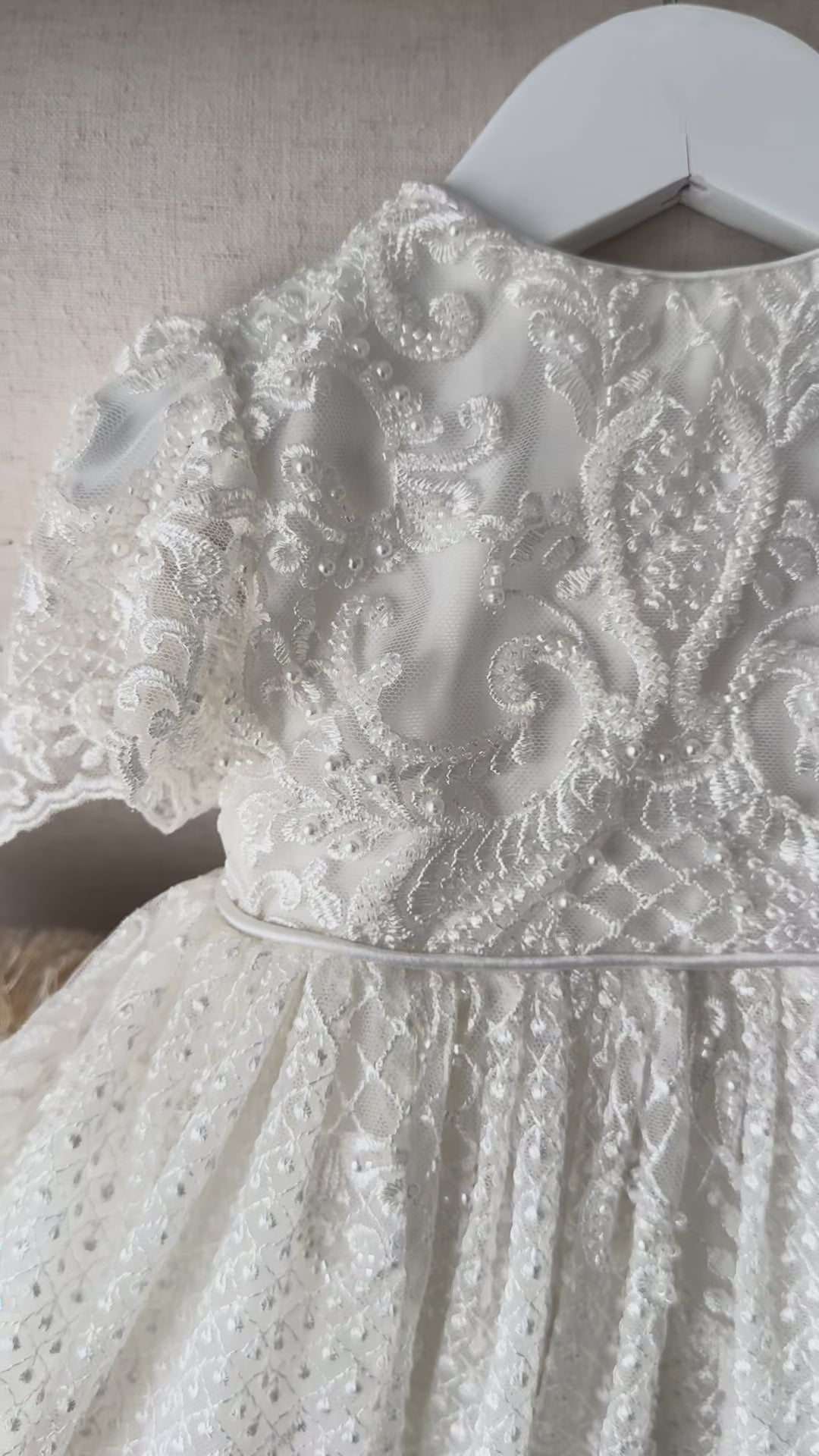 An elegant heirloom gown designed with timeless tradition in mind. Crafted from intricate lace, this gown features pearl and sequence embellishments throughout. It features delicate short sleeves, a softly structured bodice. The back is finished with delicate pearl buttons and a long mikado side belt that can be tied into a bow. The intricate lacework flows throughout the gown, creating beautiful texture and detail from every angle. 